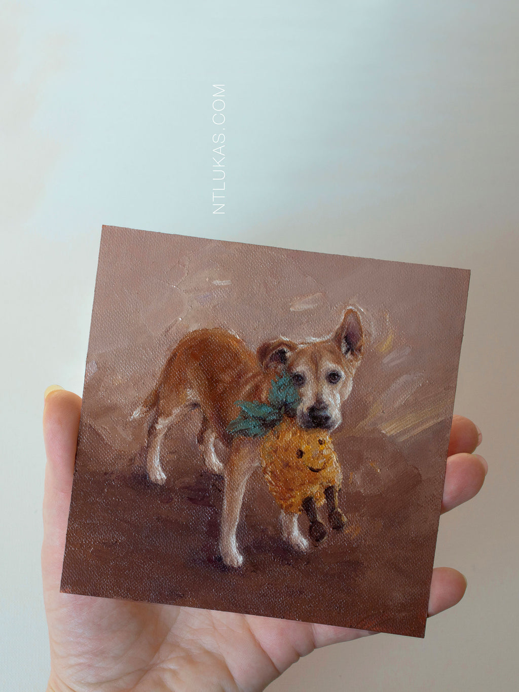 Hand holding a small square painting of a dog with a pineapple.